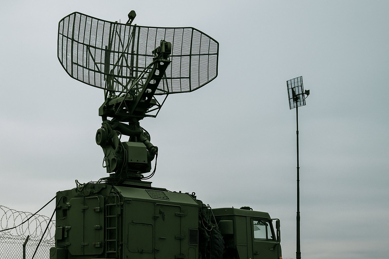 Emergency Procurement - Military radar system mounted on an olive-green vehicle, with a large rectangular dish and support antennas against a cloudy sky, used for surveillance and border security operations.